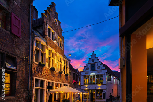 Illuminated traditional Belgian gabled houses and cafes on a charming, narrow, cobbled alley in the historic Patershol district of Ghent Belgium at twilight.