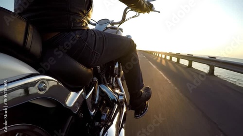 Person riding a motorcycle on a long bridge over water during a beautiful sunset.
