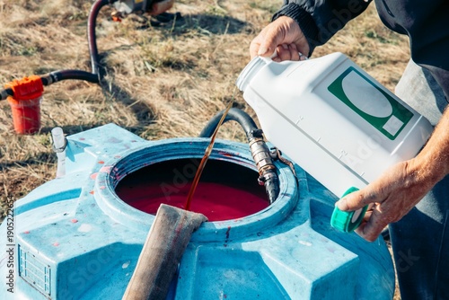 men's hands pouring chemical into a large blue plastic tank filled, agricultural mixing process, chemical transfer in sunny rural field, agriculture, irrigation, fungicides
