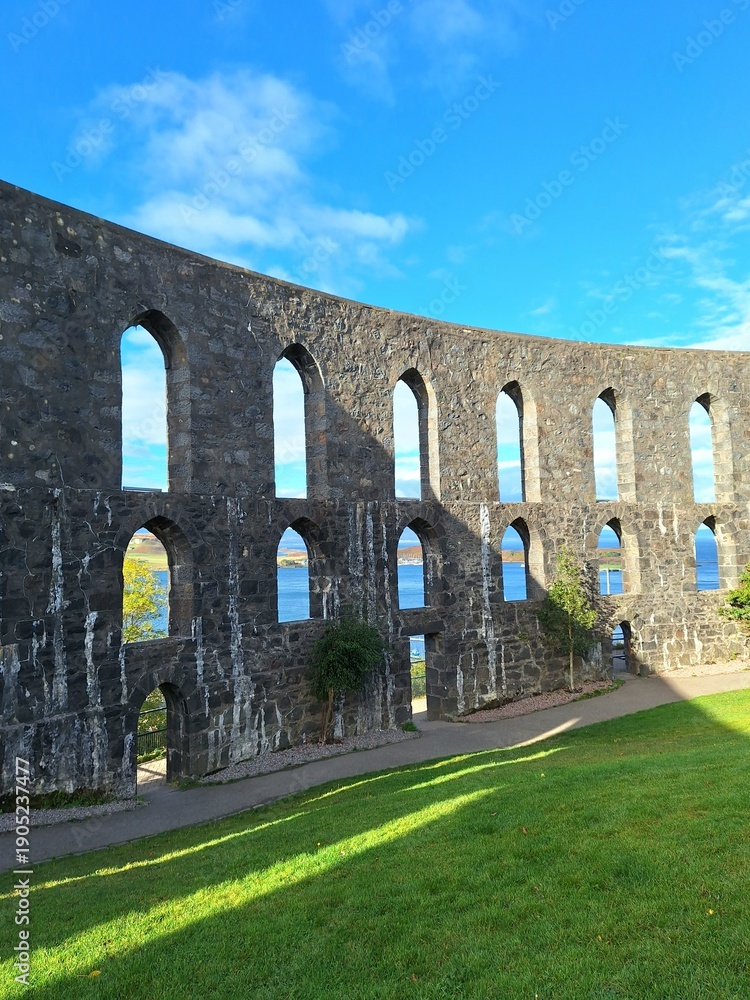 Fototapeta premium Stone arches of McCaig’s Tower in Oban, Scotland. The historic granite structure, inspired by Roman architecture, frames views of the sea and surrounding islands through its repeating arched openings.