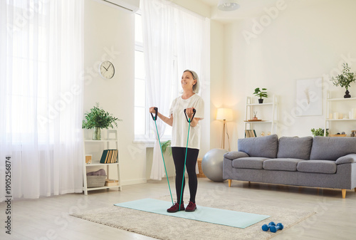 Photos Senior woman performs a stretching exercise at home gym, using fitness band for workout