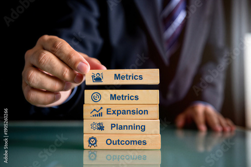 Businessman carefully stacking wooden blocks representing key business metrics expansion planning and strategic outcomes