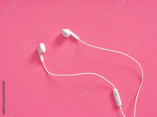 White wired earbuds resting on pink background