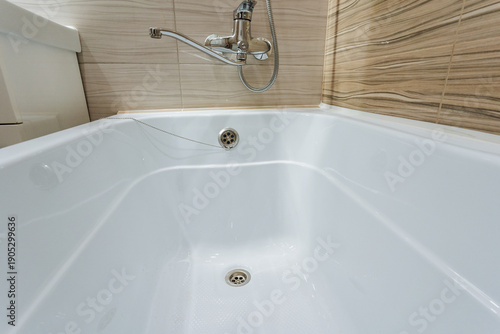 White Acrylic Bathtub Visible Drain Closeup, Glossy Beige Tiles, Hygienic Surface With Subtle Reflections, Modern Minimalist Ambience Ideal For Renovation Or Rental Listing Visuals