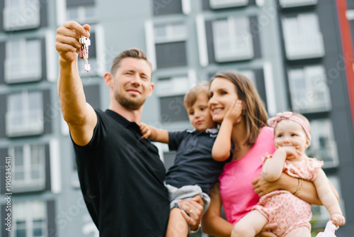 Happy Young Family with two Children Holding Keys to New Apartment Outdoors