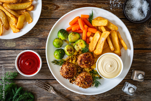 Fried pork meatballs with French fries, mini carrots and brussels sprouts on wooden table
