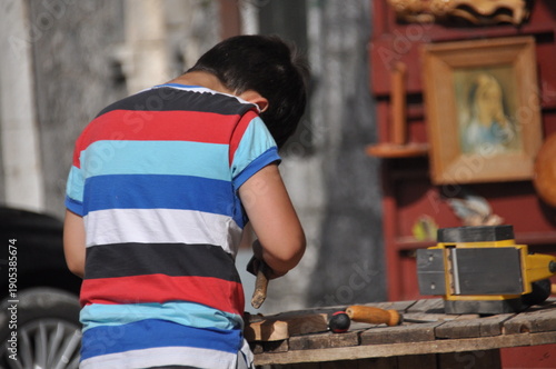 Young boy carving wood in local market under the sun on a warm afternoon