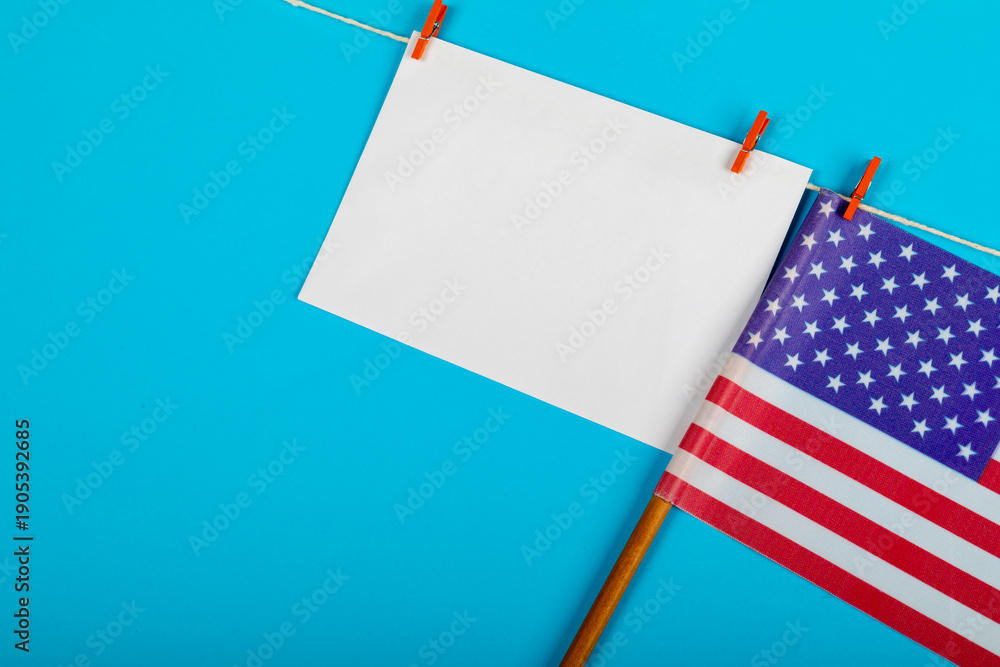 Obraz premium Blank paper with copy space hanging on clothesline besides usa flag on blue background