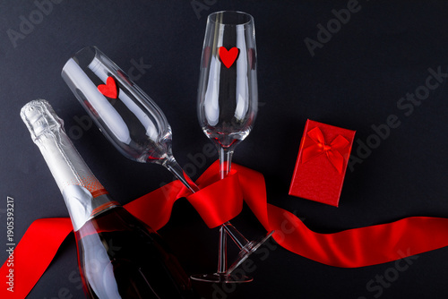 Champagne flutes tied with red ribbon by gift box and bottle on gray background, copy space