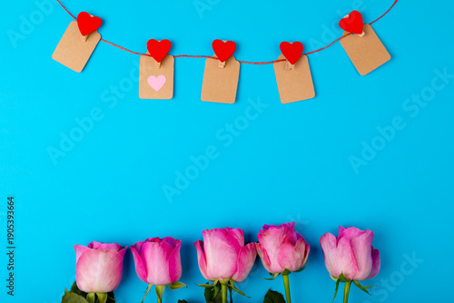 Overhead view of fresh pink roses and heart shaped decoration on blue background, copy space