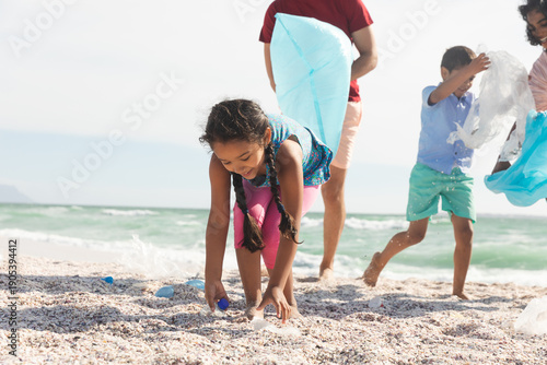 Tablou pe pânză girl collecting plastic garbage on sand at beach with family during sunny day