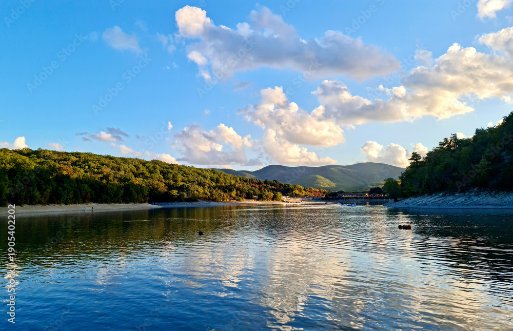 Naklejka premium Scenic sunset landscape of Sukko Lake with forested hills and blue sky reflections in the water. Anapa, Russia.