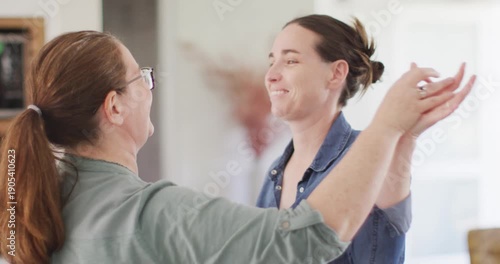 Caucasian lesbian couple smiling and dancing in kitchen