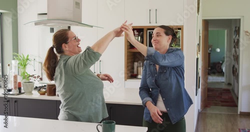 Caucasian lesbian couple smiling and dancing in kitchen