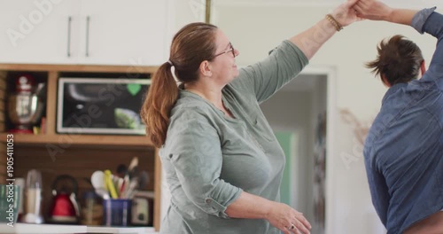 Caucasian lesbian couple smiling and dancing in kitchen