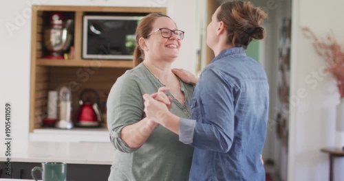 Caucasian lesbian couple smiling and dancing in kitchen