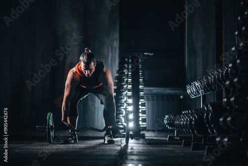 Male bodybuilder preparing barbell deadlift near dumbbell rack in gym, Man training with barbell for strength in fitness gym with dumbbell stand