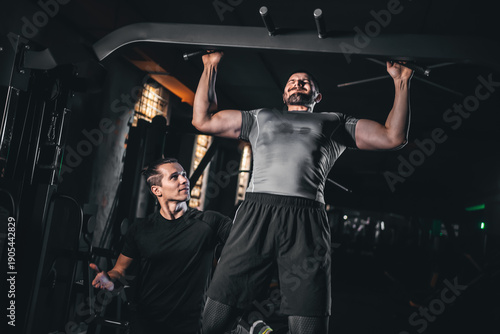 Fotografie Male bodybuilder performing lat pulldown with personal trainer in gym, Man train