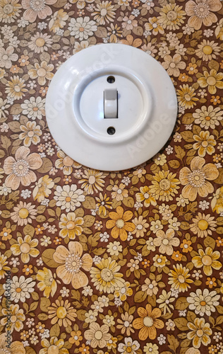 Alter runder Lichtschalter im Innenraum mit Blumenmustertapete