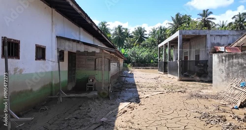 Flooded village street with damaged buildings and mud.
