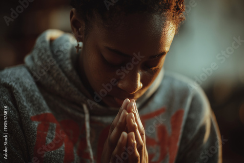 Teen praying in hoodie with bowed head and warm light showing deep faith and connection to Christian spirituality