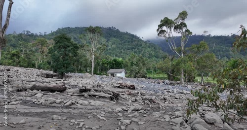 Dry riverbed with rocky terrain and lush green mountains in the background under a cloudy sky.