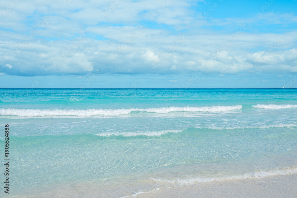 Obraz premium Calm ocean waves gently lap on the sandy shore under a bright blue sky