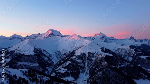 Snowy mountain peaks illuminated by vibrant pink sunrise with blue sky