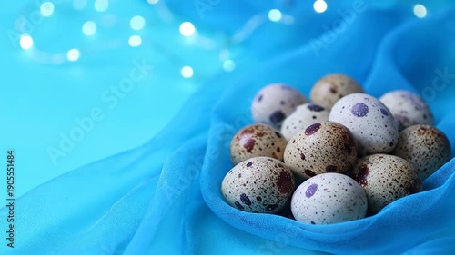 Speckled quail eggs rest in blue fabric, set against a soft, bright turquoise backdrop