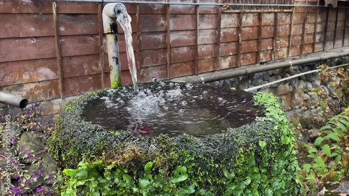 Water pours from hosepipe into mossy fountain basin in Tsumago Japan