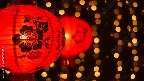 Two vibrant red, floral paper lanterns glow brightly against a bokeh of yellow lights