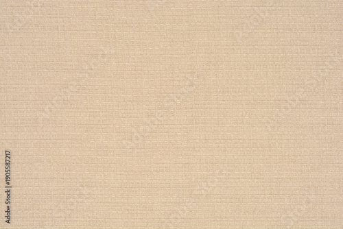 A full frame shot of a beige waffle weave fabric displaying a uniform square grid pattern with natural cotton fiber details
