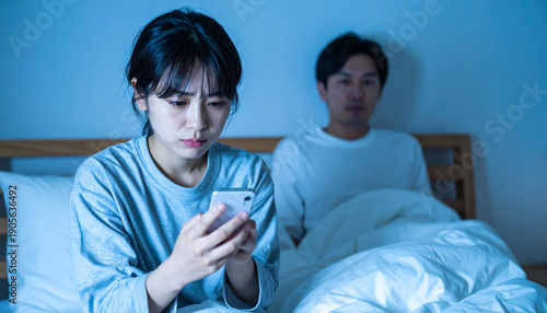 寝室で携帯を見る妻