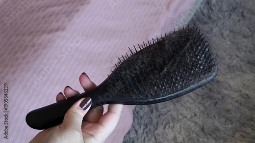 Dark hair falling out on a hair comb in a woman's hand close-up. Hair loss