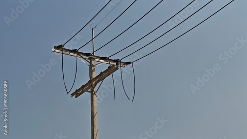 Foto Broken high voltage electrical power line jumper wire hanging from concrete pole causing blackout and danger risk against grey sky