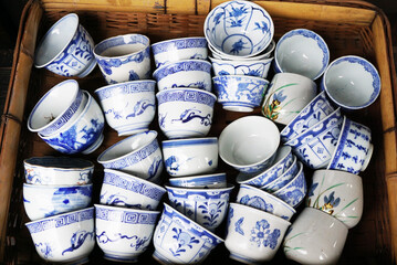 Assorted traditional Japanese ceramic teacups with blue patterns in a bamboo basket.