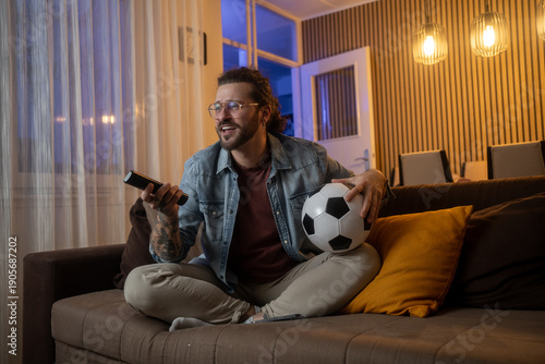 Man holding a soccer ball cheering while watching sports on TV at home