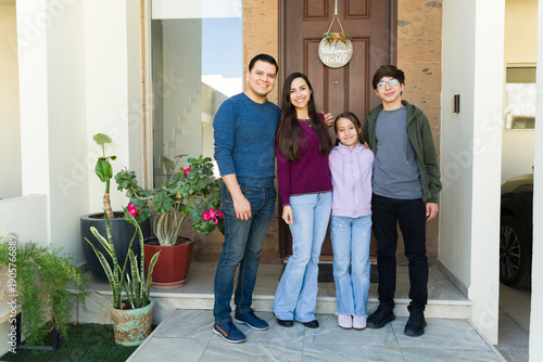 Tableau sur toile Happy latin family standing on porch in front of their new home, smiling and fee
