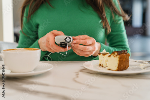 Mid-section view of a woman adjusting her insulin pump bolus before enjoying a cheesecake and coffee in a bright cafe.