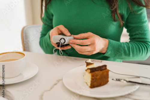 Close-up of a woman with type 1 diabetes using an insulin pump to calculate a meal dose while sitting at a cafe table. Mindful nutrition and insulin pump therapy in daily life.