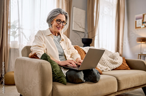 Smiling senior woman working on laptop from home in a cozy living room.