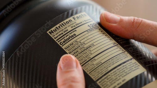 Close-up shot of a black jar of whey protein powder with nutrition facts label in person hands.