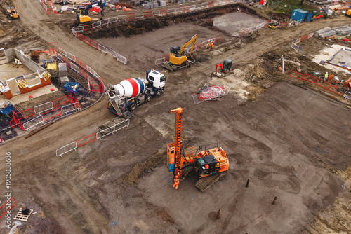 Aerial view from drone at Drilling auger piling rig operating on site near new housing development while workers manage tasks under cloudy skies