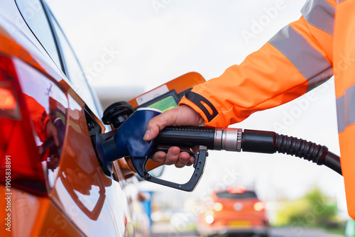 Close-up of a Man refuelling orange car at gas fuel station. Male filling diesel at petrol station using a fuel nozzle