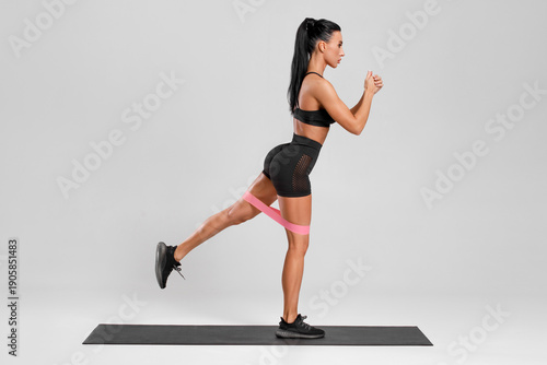 Fitness woman doing exercise for glutes with resistance band on gray background. Athletic girl working out