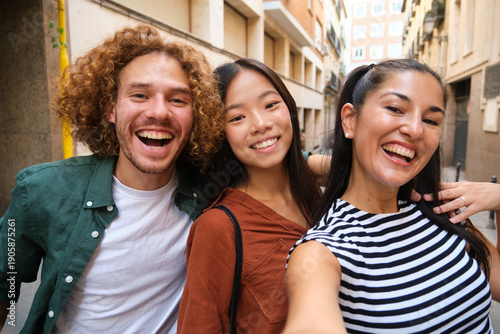 Three cheerful multi ethnic friends are taking a selfie while walking in a city street