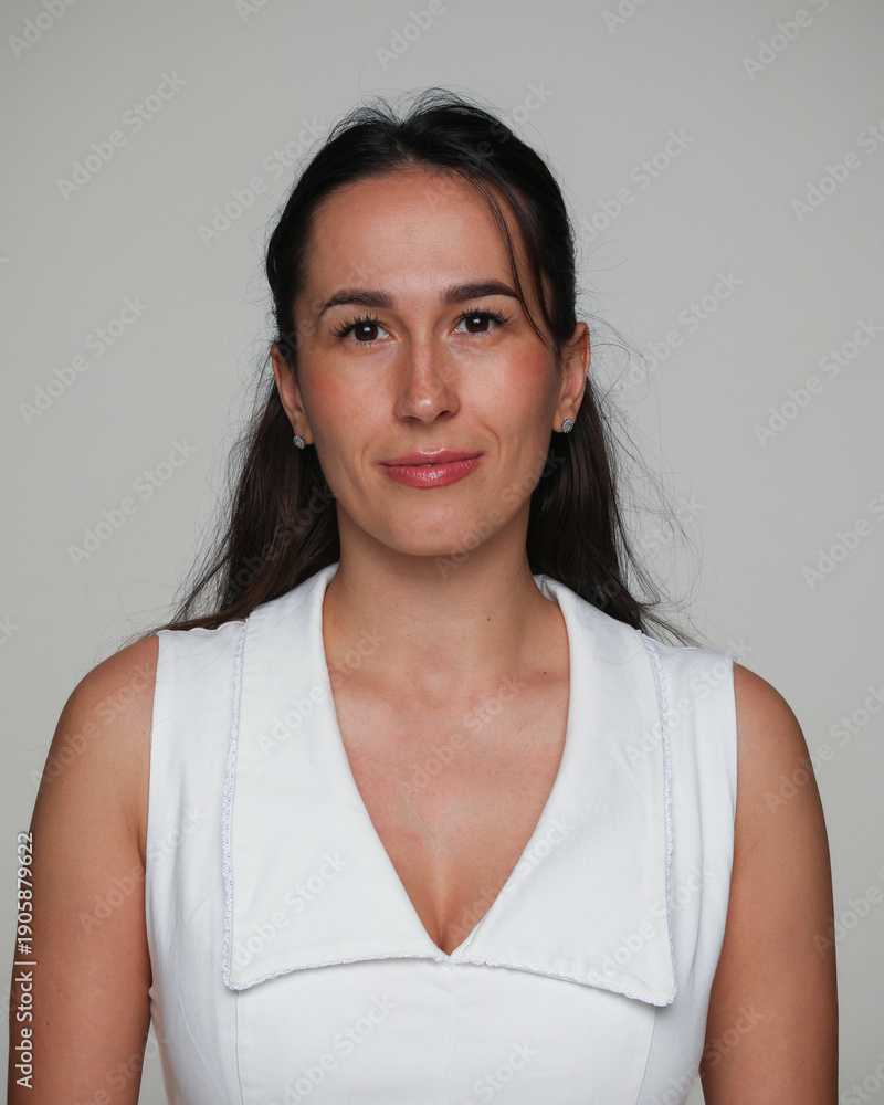Obraz premium Front image closeup of a brunette young woman with make-up, in a dress, posing in studio, over grey background. 