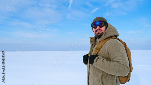 Φωτογραφία Man wearing a winter hat, protective goggles, and a warm jacket carrying a backp