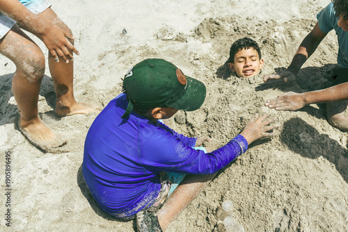 Three boys playing and having fun burying a friend in the sand on a summer beach