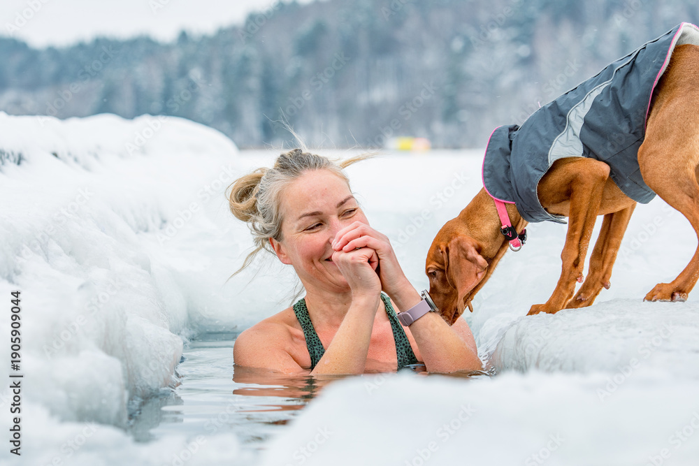 Φωτογραφία Beautiful blonde hair woman with her dog immersed in the freezing cold water of a lake practicing cold water swimming